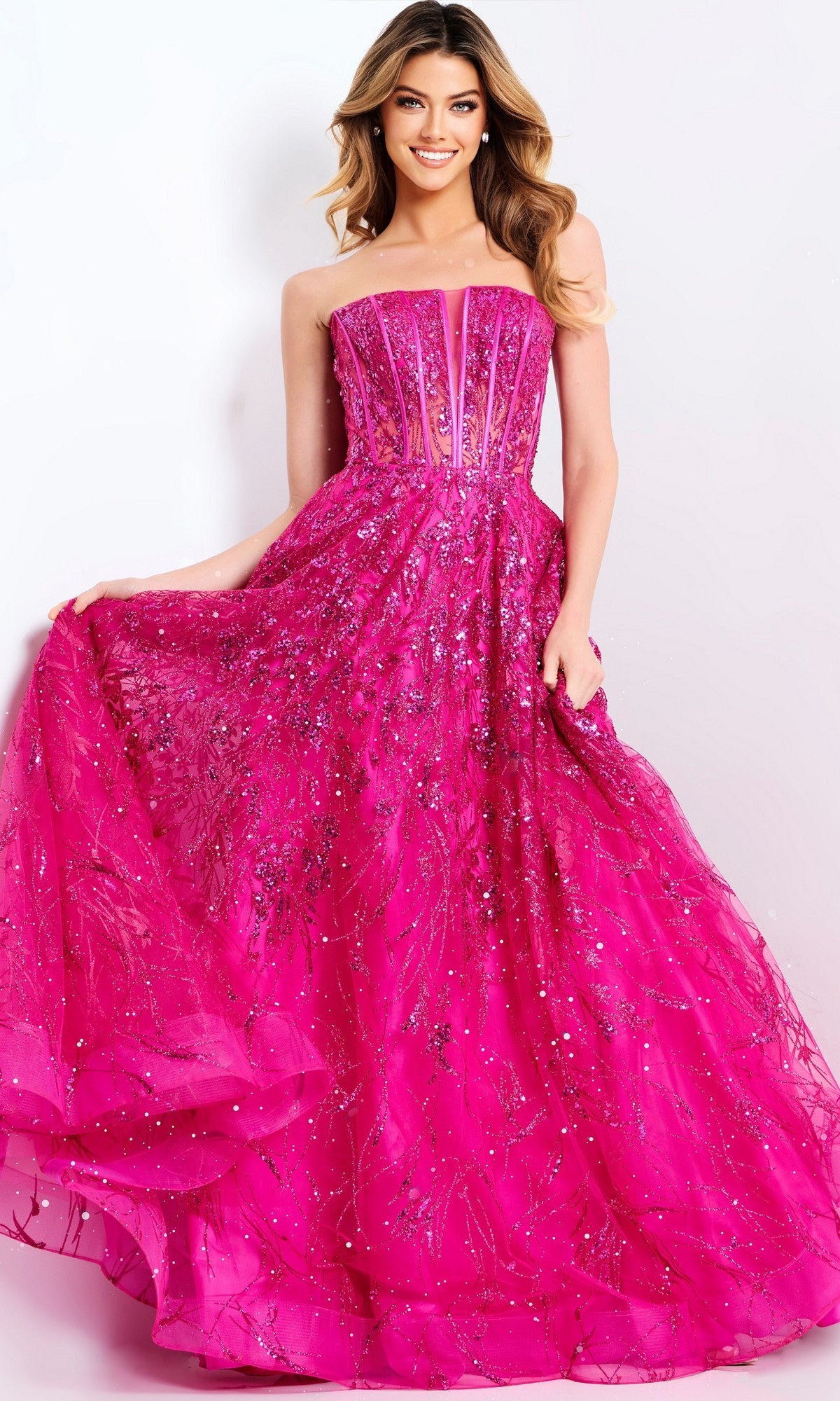 Woman in the Jovani 45913 long prom dress, featuring a strapless bright pink sequin corset bodice, smiles while holding out the skirt against a plain background.